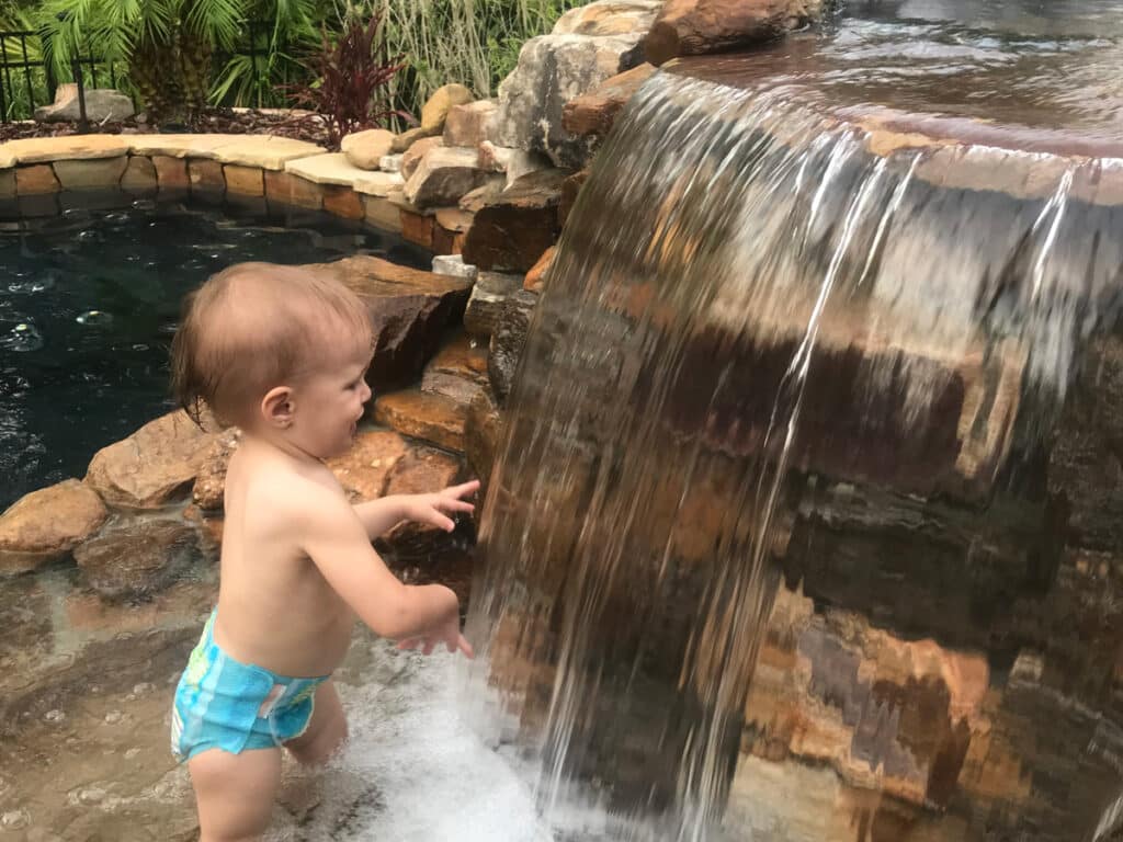 Baby plays in a waterfall leading into an Immerspa inground hot tub