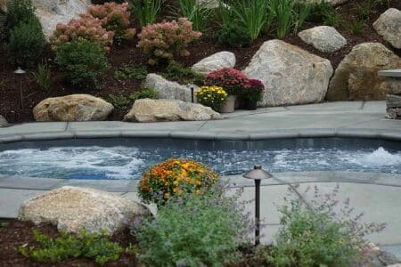 Swim Spa vs a Regular Spa | Spa in backyard with natural rock wall and gardens surrounding | Immerspa - The Best Fiberglass Inground Spas, Hot Tubs, & Pools